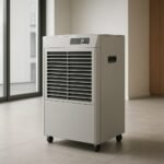 A modern commercial dehumidifier on wheels positioned in a bright, minimalistic room with large windows.